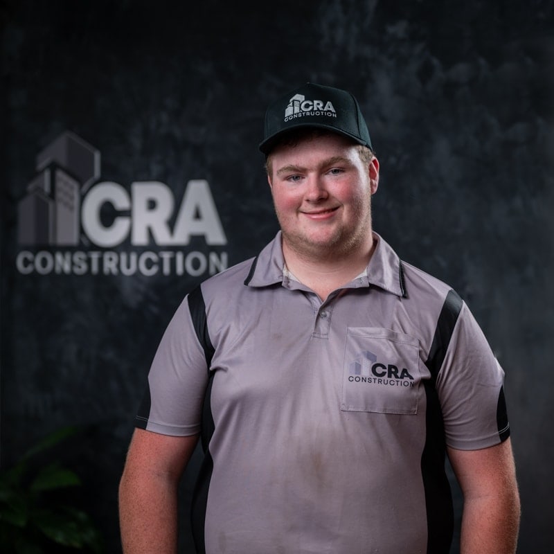 A man in a Brisbane plasterer uniform and cap, smiling against a background with a blurred Brisbane plasterer logo.