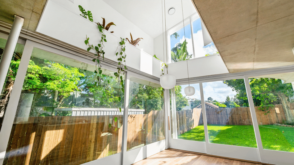 Sunroom with expansive glass windows showcasing a green backyard and natural light.